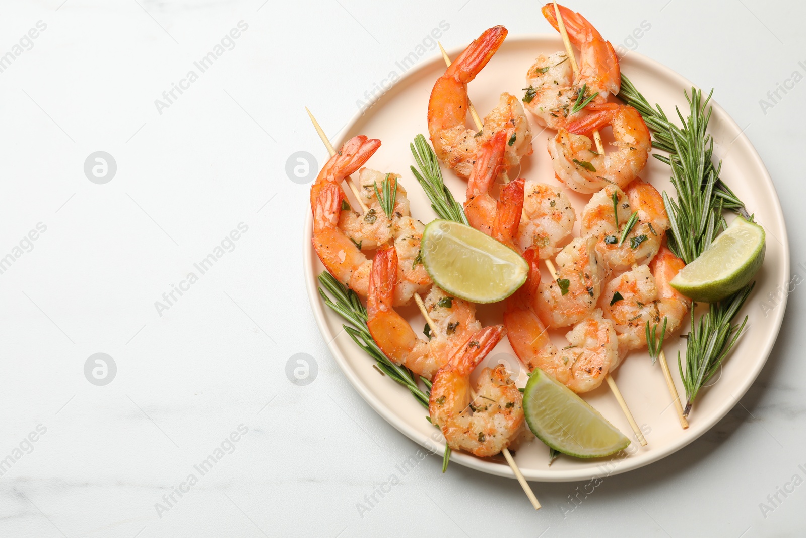 Photo of Skewers with delicious grilled shrimps served on white table, top view. Space for text