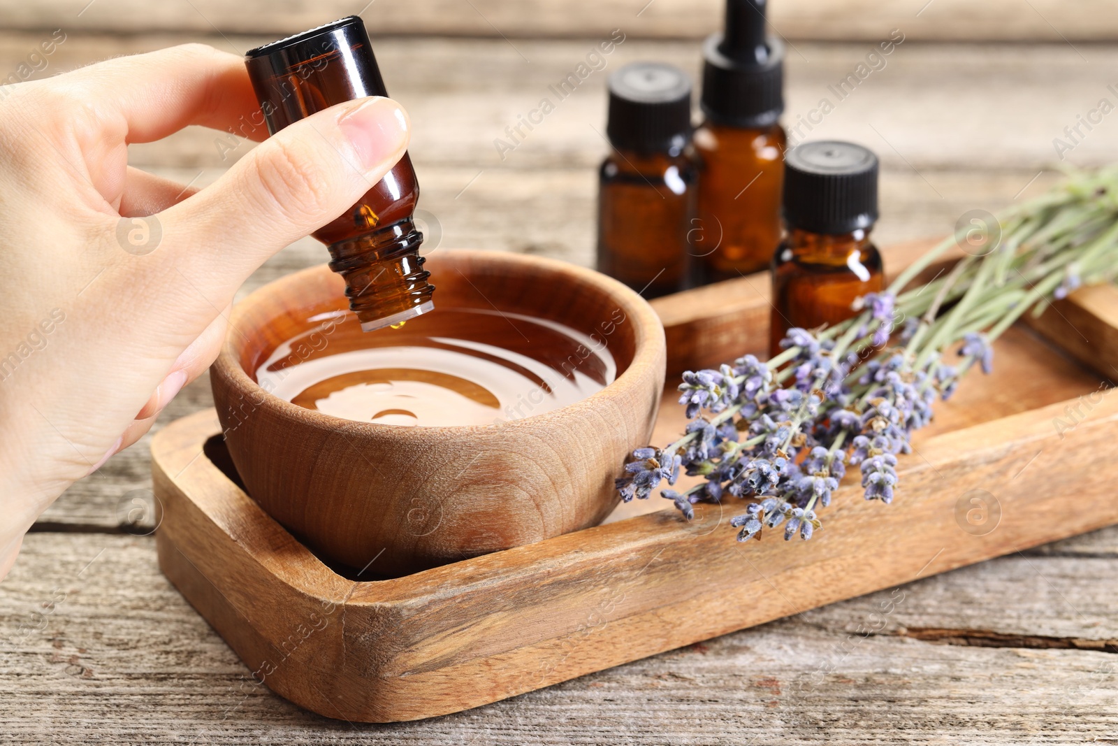 Photo of Woman dripping essential oil into bowl with water at wooden table, closeup