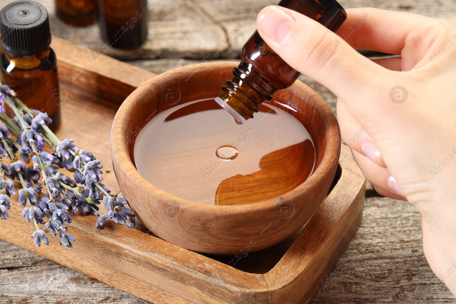 Photo of Woman dripping essential oil into bowl with water at wooden table, closeup