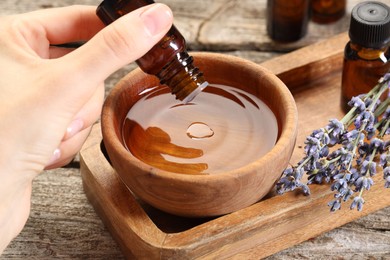 Photo of Woman dripping essential oil into bowl with water at wooden table, closeup