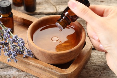 Woman dripping essential oil into bowl with water at wooden table, closeup