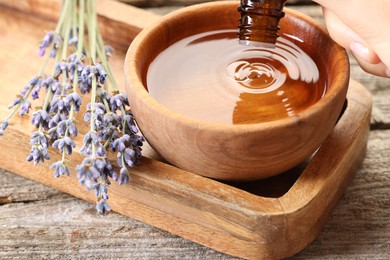 Woman dripping essential oil into bowl with water at wooden table, closeup