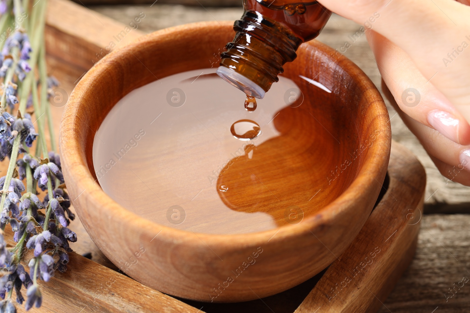 Photo of Woman dripping essential oil into bowl with water at wooden table, closeup