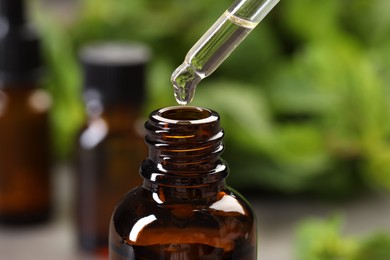 Dripping essential oil into bottle on blurred background, closeup