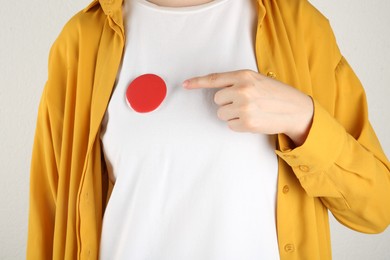 Woman with blank red button badge on light background, closeup