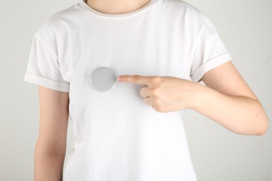 Woman with blank grey button badge on light background, closeup