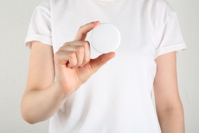 Woman with blank white button badge on light background, closeup