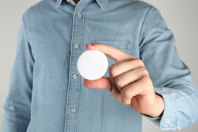 Woman with blank white button badge on light background, closeup