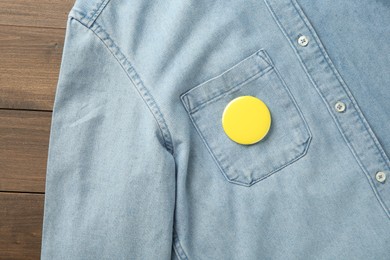 Photo of Denim shirt with blank button badge on wooden background, top view. Mockup for design