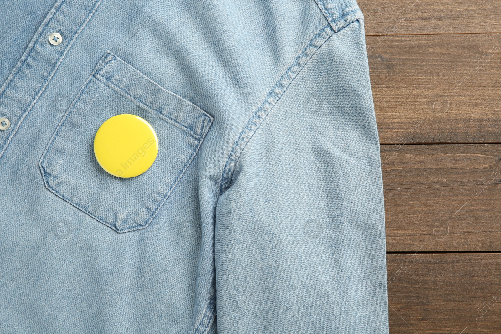 Photo of Denim shirt with blank button badge on wooden background, top view. Mockup for design