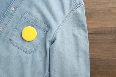 Photo of Denim shirt with blank button badge on wooden background, top view. Mockup for design