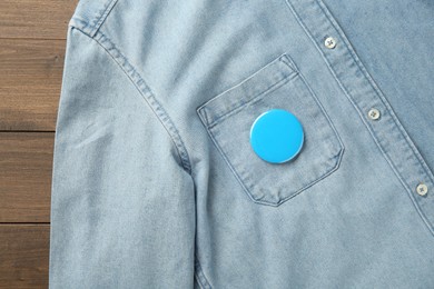 Denim shirt with blank button badge on wooden background, top view. Mockup for design