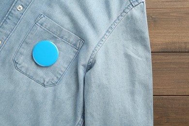 Photo of Denim shirt with blank button badge on wooden background, top view. Mockup for design