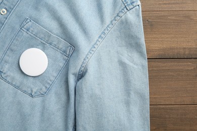 Denim shirt with blank button badge on wooden background, top view. Mockup for design