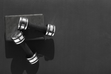 Dumbbells and yoga block on black mat, flat lay. Space for text