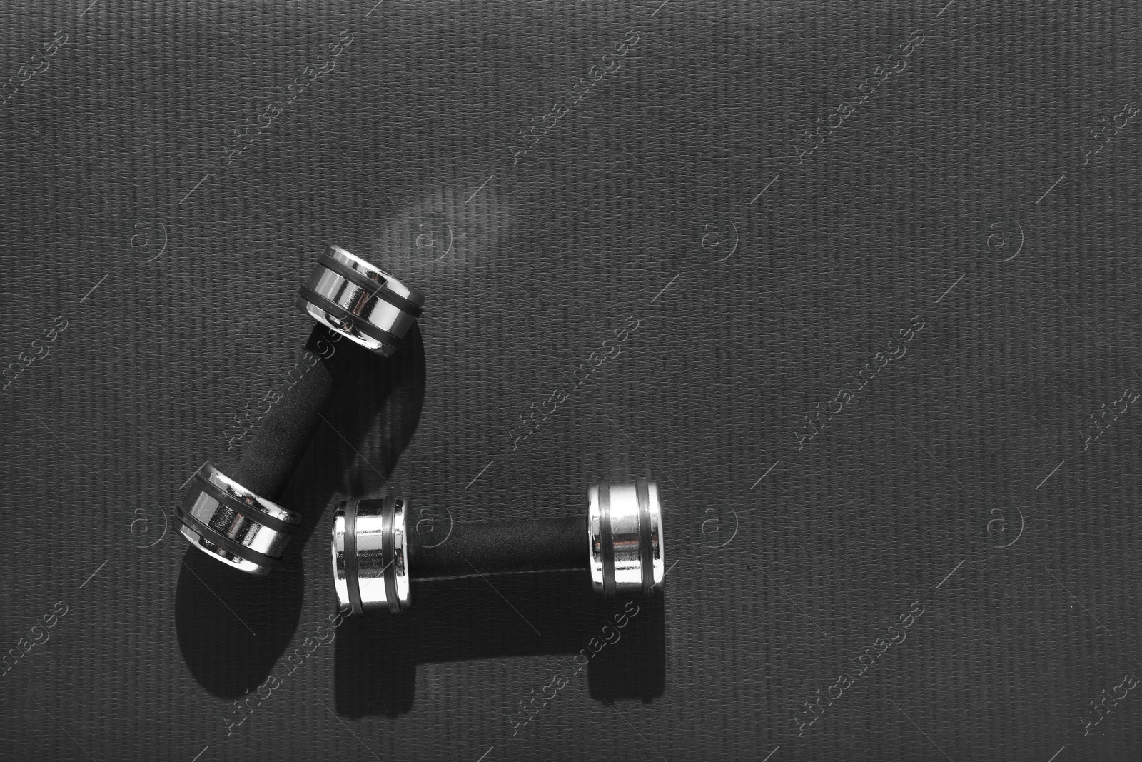 Photo of Dumbbells on black yoga mat, top view. Space for text