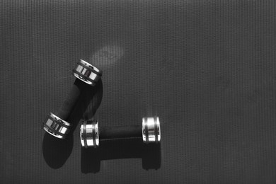 Dumbbells on black yoga mat, top view. Space for text