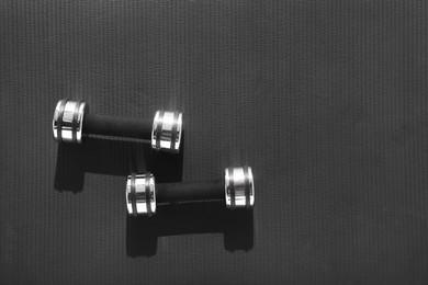 Dumbbells on black yoga mat, top view. Space for text