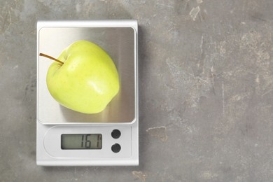 Photo of Kitchen scale with apple on grey textured table, top view. Space for text