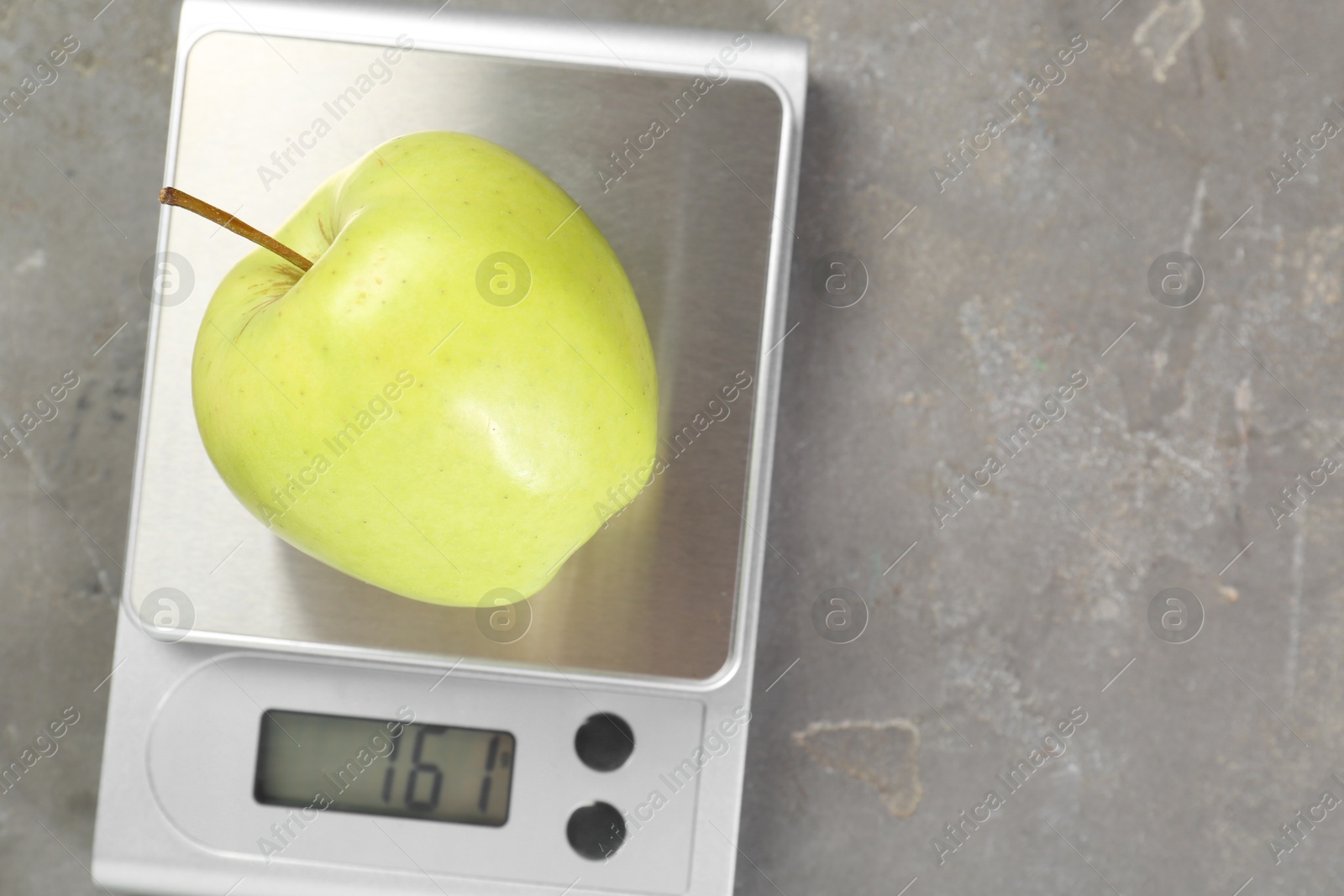 Photo of Kitchen scale with apple on grey textured table, top view. Space for text