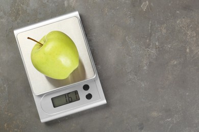 Photo of Kitchen scale with apple on grey textured table, top view. Space for text