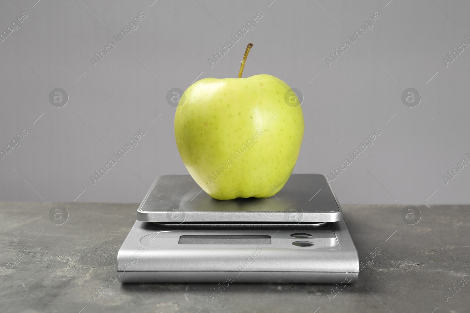 Photo of Kitchen scale with apple on grey textured table, closeup