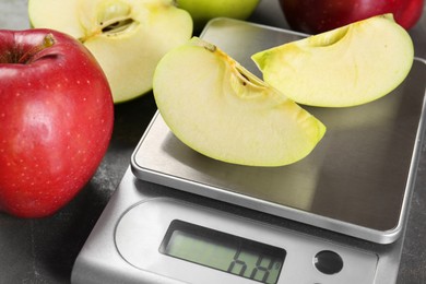 Photo of Kitchen scale with pieces of apple and fruits on grey textured table, closeup