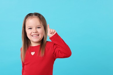 Photo of Portrait of happy little girl pointing at something on light blue background, space for text