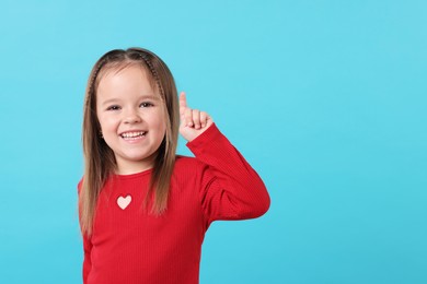 Portrait of happy little girl pointing at something on light blue background, space for text