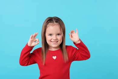 Photo of Portrait of happy little girl showing OK gesture on light blue background