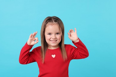 Portrait of happy little girl showing OK gesture on light blue background