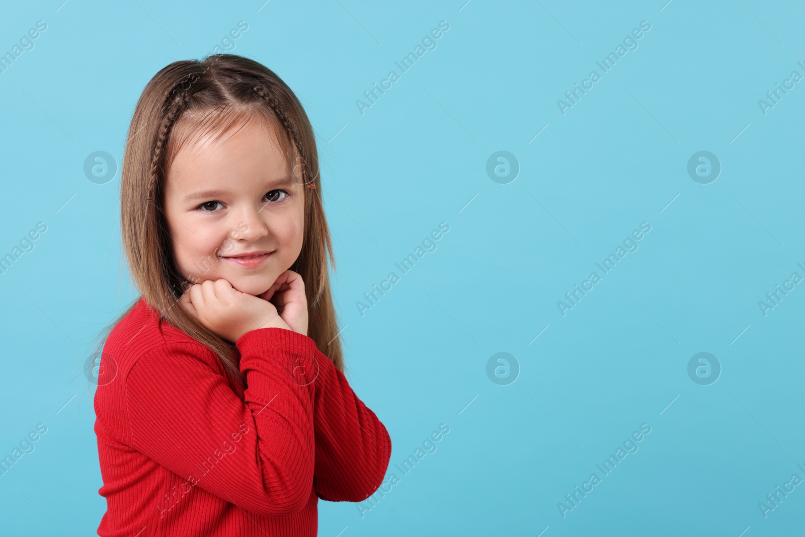 Photo of Portrait of cute little girl on light blue background, space for text