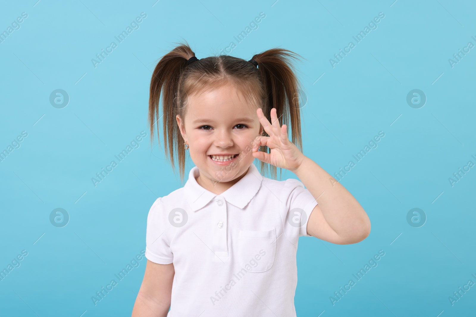 Photo of Portrait of happy little girl showing OK gesture on light blue background