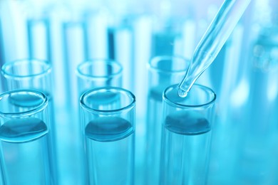 Photo of Dripping liquid from pipette into test tube on light blue background, closeup