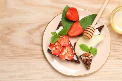 Photo of Delicious bruschettas with fresh ricotta (cream cheese), strawberry, mint and pear served with honey on wooden table, flat lay. Space for text