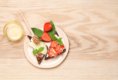 Photo of Delicious bruschettas with fresh ricotta (cream cheese), strawberry, mint and pear served with honey on wooden table, flat lay. Space for text