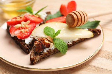 Photo of Delicious bruschettas with fresh ricotta (cream cheese), strawberry, mint and pear served with honey on wooden table, closeup