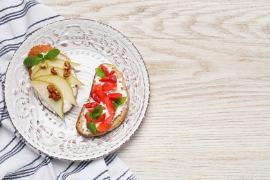 Photo of Delicious bruschettas with fresh ricotta (cream cheese), strawberry, mint and pear on wooden table, top view. Space for text