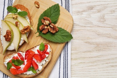 Delicious bruschettas with fresh ricotta (cream cheese), strawberry, mint and pear on wooden table, top view. Space for text