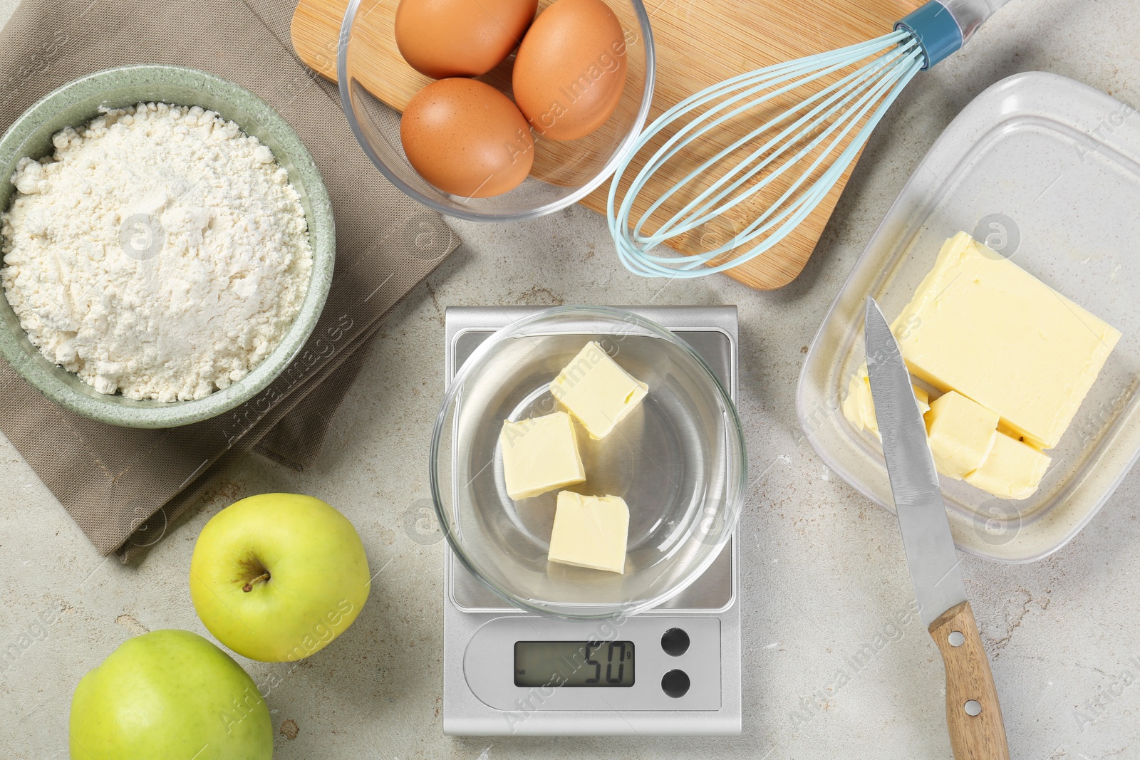 Photo of Kitchen scale with bowl of butter and other products on grey table, flat lay