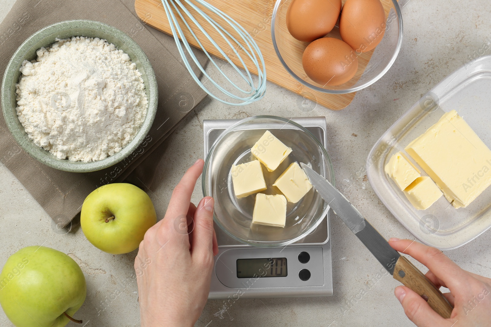 Photo of Woman weighing butter on kitchen scale at grey table, top view