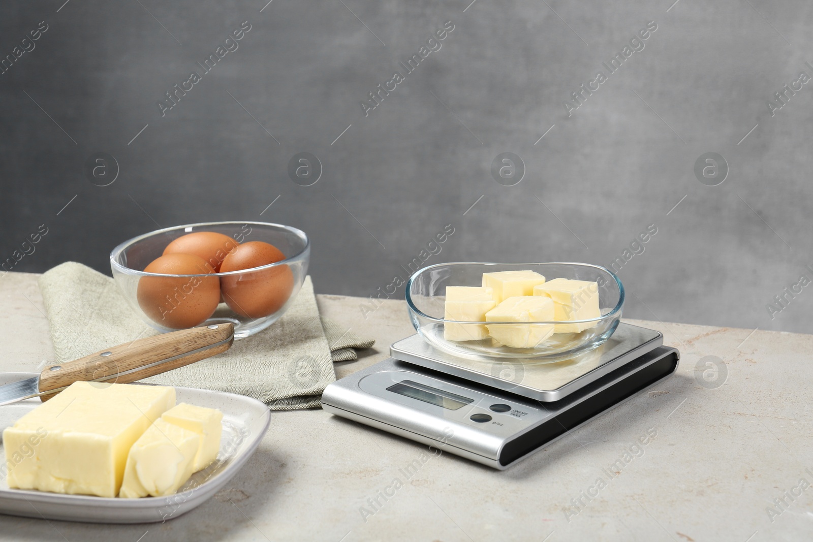 Photo of Kitchen scale with bowl of butter and other products on grey table, space for text