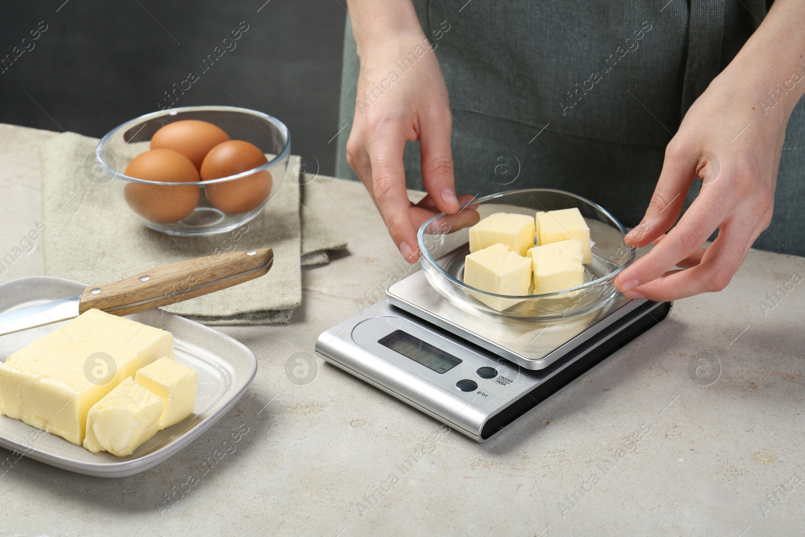 Photo of Woman weighing butter on kitchen scale at grey table, closeup