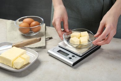 Photo of Woman weighing butter on kitchen scale at grey table, closeup