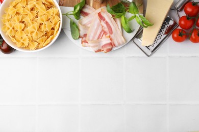 Photo of Raw pasta and fresh ingredients on white tiled table, flat lay. Space for text