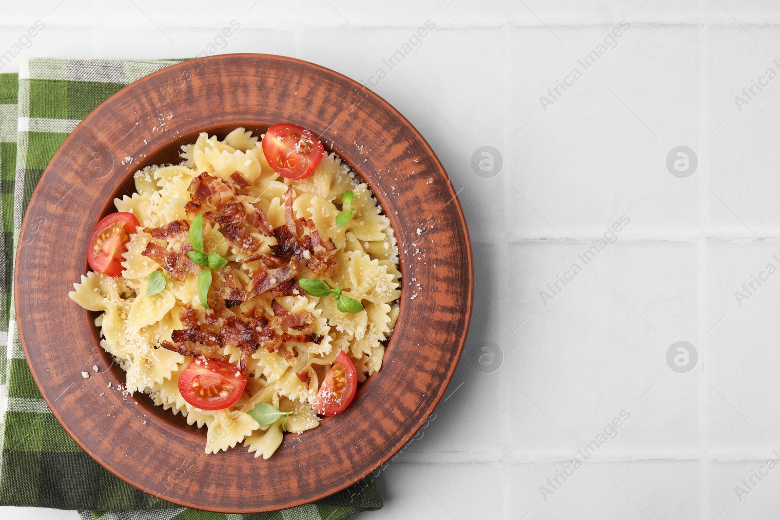 Photo of Tasty pasta with bacon, tomatoes and basil on white tiled table, top view. Space for text