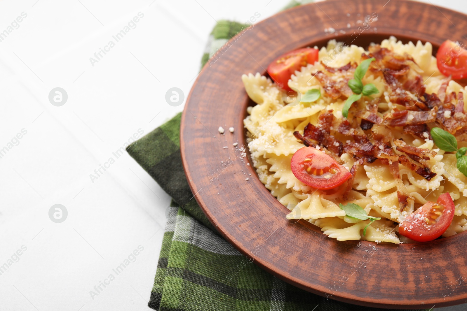 Photo of Tasty pasta with bacon, tomatoes and basil on white tiled table, space for text