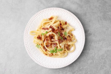 Tasty pasta with bacon and basil on light grey table, top view