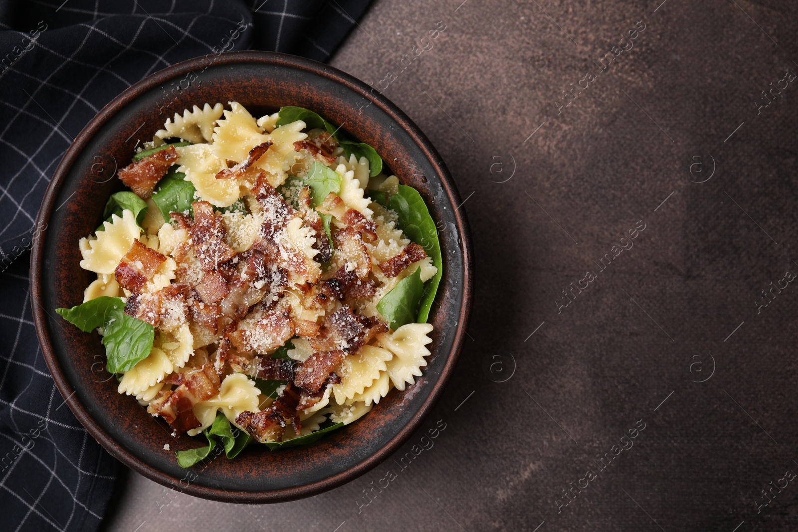 Photo of Tasty pasta with bacon and basil on brown table, top view. Space for text