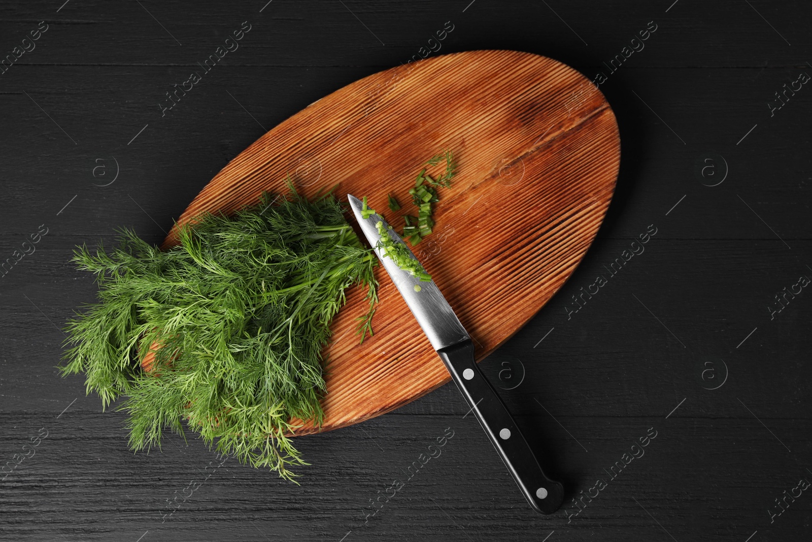 Photo of Sprigs of fresh green dill and knife on black wooden table, top view